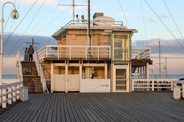 Sopot, Polonya - 7 Ekim 2024: Uzun tahta iskelenin sonunda oldukça büyük bir bina var. Gdansk Körfezi 'ndeki iskele, Baltık Denizi turistler ve şehir sakinleri tarafından hevesle ziyaret ediliyor..