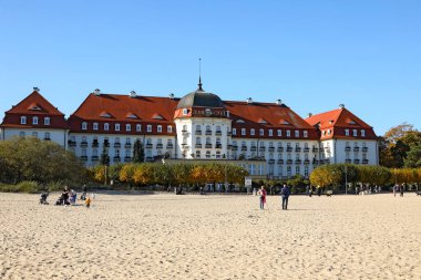 Sopot, Polonya - 12 Ekim 2024: 5 yıldızlı Sofitel Grand Sopot Oteli Gdansk Körfezi 'nin kumlu sahilinin kenarında yer almaktadır. Otel binası 1927 'den kalma. İnsanlar sahilde dinleniyor.