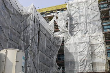 Varşova, Polonya - 9 Mart 2025: Yeni bir apartmanın inşaatı. Plastik ağ işçileri korumak ve güvenliklerini artırmak için binanın etrafındaki iskeleleri örtmek için kullanılır.