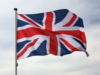 Bulutlu bir gökyüzünde, Birleşik Krallık bayrağı dalgalanır bayrak direğinde.