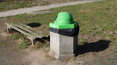 Yeşil kapaklı beton bir çöp tenekesi eski bankın yanındaki çimenliğe yerleştirilir. Dar yol yakınlarda. Bu manzara ayrıntıları Polonya 'nın Varşova kentindeki Goclaw konutlarında..