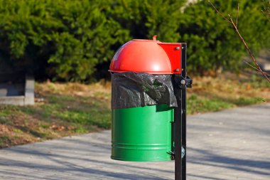 Kırmızı kapaklı yeşil metal bir çöp tenekesi ve siyah bir plastik torba Goclaw 'daki konutların kaldırımının yanında, Varşova, Polonya.