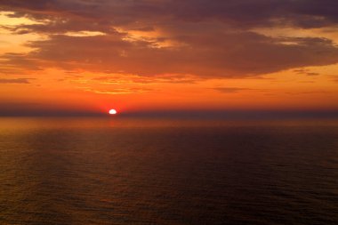 Batan güneş, Baltık Denizi üzerinde ufka ulaştı. Gökyüzü turuncu ve kırmızıya boyandı. Deniz gün batımının renkleriyle koyu kırmızı görünüyor. Görüntü: Ustronie Morskie Köyü, Polonya.