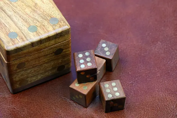Zar şeklinde tahta bir kutu. Yanında da daha küçük tahta zarlar var. Deri bir yüzey üzerinde. Bu tema çeşitli finansal, oyun, şans ve risk temaları için kullanılabilir.
