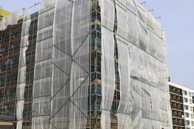 Varşova, Polonya - 9 Mart 2025: Yeni bir apartmanın inşaatı. Plastik ağ işçileri korumak ve güvenliklerini artırmak için binanın etrafındaki iskeleleri örtmek için kullanılır..