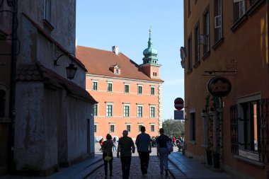 Varşova, Polonya - 4 Nisan 2025: Dar bir Piwna caddesinden görülen Kraliyet Kalesi 'nin bir parçası. Dört kişi caddeden kaleye doğru yürüyor..