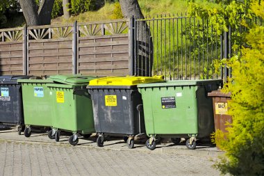 Mielno, Polonya - 20 Mayıs 2025: Atık toplama ve ayrımcılık sepetleri farklı renklerdedir ve kaldırıma bir çite karşı yerleştirilmiştir.