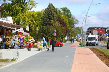 Mielno, Polonya - 15 Mayıs 2025: Sokak boyunca uzanan bir kaldırım ve bisiklet yolu, evler ve birçok bitki örtüsüyle kaplı. Bir oyuncakçı dükkânı kenarda duruyor, mallarıyla ziyaretçileri cezbediyor..