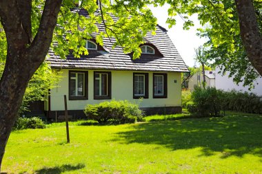 Mielno, Polonya - 12 Mayıs 2025: Bu sahil kasabasında geleneksel bir ev yeşil çimenler ve ağaçlarla çevrilidir. Çatı seramik fayanslarla kaplı..