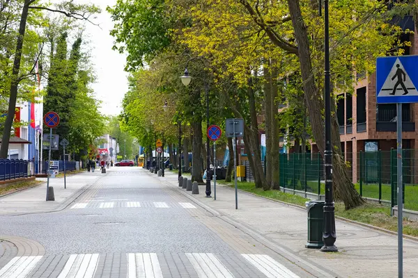 Mielno, Polonya - 13 Mayıs 2025: Kombine bir cadde sahil kasabasından geçiyor. Sokağın iki tarafında da sıra sıra sıra ağaçlar var. Yolda neredeyse hiç trafik yok..