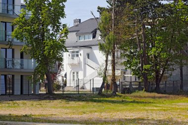 Mielno, Polonya - 13 Mayıs 2025: Bir deniz kentinde iki farklı bina kısmen görülebilir. Çimlerin kenarında büyüyen ağaçlar onları daha da gizliyor..