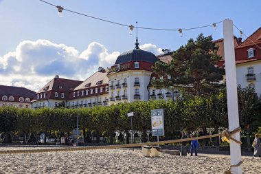 Sopot, Polonya - 6 Ekim 2024: 5 yıldızlı Sofitel Grand Sopot Oteli Gdansk Körfezi 'nin kumlu sahilinin kenarında yer almaktadır. Otel binası 1927 'den kalma. İnsanlar sahilde dinleniyor.