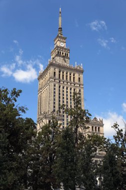 Varşova, Polonya - 30 Haziran 2025: Ağaçların üzerinde 237 metrelik Kültür ve Bilim Sarayı 'nı görebilirsiniz. Saray birçok şirket ve kamu kuruluşuna ev sahipliği yapar..