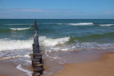 Mandıra ve ona vuran dalgalar, Polonya 'nın Mielno kentindeki Baltık Denizi kıyıları boyunca görülebilir. Dalgaların zararlı etkilerinden korunmak için dalgalar deniz tabanına doğru sürüklenir..