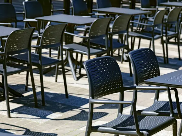 Kaldırımdaki kafedeki masalar ve sandalyeler siyah. Koltuklar boş ve dolu değil..