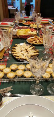 Noel atmosferi için kırmızı ve yeşil kareli masa örtüsüyle kaplanmış masa örtüsü, cam eşyalar ve sofra takımı, uzaya canlı ve neşeli bir dokunuş katıyor.