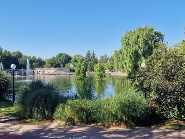 Sakin göl manzaralı açık bir günde hafif dalgalar etrafındaki kayaları ve çimenli kıyıları yansıtıyor.