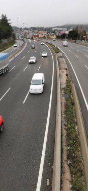 Otoyol arabalar ve kamyonlarla dolu, sürekli bir trafik akışı gösteriliyor