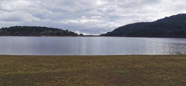 Sakin göl manzaralı açık bir günde hafif dalgalar etrafındaki kayaları ve çimenli kıyıları yansıtıyor.