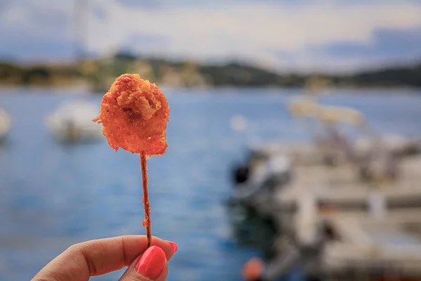 Crispy shrimp fritter on a stick with Mediterranean Sea and boats in background, Villefranche sur Mer Old Town on the French Riviera, South of France