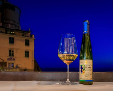 Manarola, İtalya - 31 Mayıs 2022: Akdeniz manzaralı bir restoranda şişe ve bir bardak geleneksel Cinque Terre Sciacchetra tatlı beyaz şarap