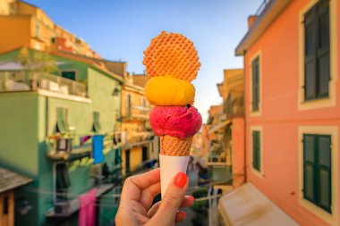 Manarola 'nın eski bir kasabası olan Cinque Terre, İtalya' daki geleneksel renkli evlerin manzarası ve kurabiyeli zanaatkar bir dondurmayı elinde tutan bir kadın.