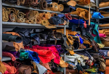 Colorful rolls of leather and fabric on shelves in the back of a traditional artisanal leather workshop and studio in Centro Storico, Florence, Italy