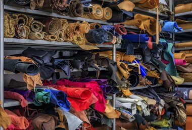 Colorful rolls of leather and fabric on shelves in the back of a traditional artisanal leather workshop and studio in Centro Storico, Florence, Italy