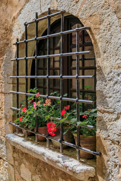 Metal bars and potted flowers on an arched old stone house window in the medieval town of Saint Paul de Vence, French Riviera, South of France