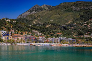 Güneşli bir günde, Fransa 'nın güneyinde, Fransız Rivierası' nda, Menton 'un Vieille Ville kasabasındaki Akdeniz ve plajın yukarısındaki renkli ev cepheleri.