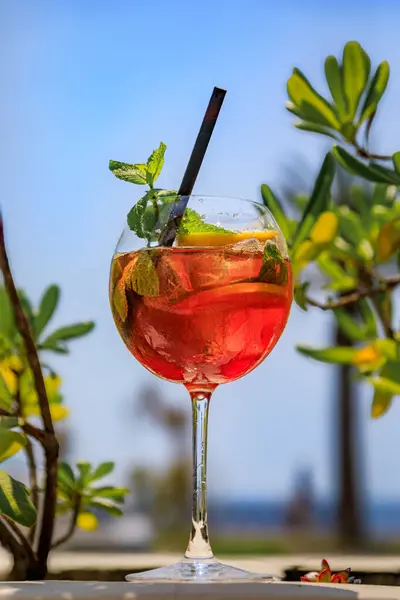 A fancy cocktail on a table at an outdoor bar on Promenade des Anglais with a background of palm trees and Mediterranean Sea in Nice, France