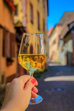 Bir açık hava restoranında bir bardak beyaz şarapla bir kadın eli Riquewihr, Fransa 'da Alsatian Wine Route' daki bir köyde yarım yamalak ahşap evler bulanıklaştırdı.