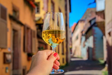Bir açık hava restoranında bir bardak beyaz şarapla bir kadın eli Riquewihr, Fransa 'da Alsatian Wine Route' daki bir köyde yarım yamalak ahşap evler bulanıklaştırdı.