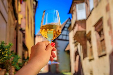 Bir açık hava restoranında bir bardak beyaz şarapla bir kadın eli Riquewihr, Fransa 'da Alsatian Wine Route' daki bir köyde yarım yamalak ahşap evler bulanıklaştırdı.