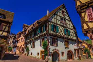 Riquewihr, Fransa - 2 Haziran 2023: Alsatian Şarap Yolu 'ndaki popüler bir köyde süslü ve renkli geleneksel yarı ahşap evlerdeki dükkanlar