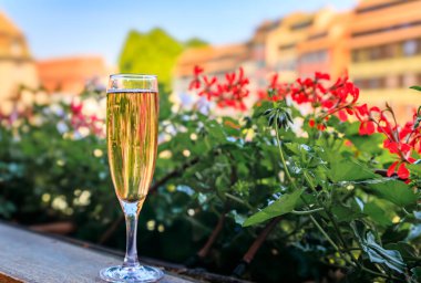 Fransa 'nın Strazburg bölgesinin Petite France bölgesinde arka planda çiçekli geleneksel bir şarap koçanında bir bardak Cremant köpüklü şarap.