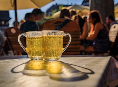 Açık hava restoranındaki bir masada iki kupa köpüklü elma şarabı, arka planda bulanık müşteriler, Petite France, Strasbourg, Fransa