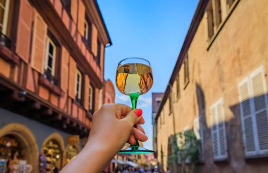 Açık hava restoranında bir bardak Gewurztraminer şarabı ile bir kadının eli, Colmar France, Alsace Wine Route köyündeki yarım tahtalı evleri bulanıklaştırdı.