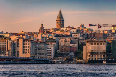 İstanbul, Türkiye 'de gün batımının altın saatinde Galata Kulesi ile Galata Köprüsü' nün yanındaki İstanbul Boğazı 'nın karşısındaki Karaköy bölgesinin gündoğumu manzarası