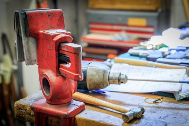 Kaliforniya 'da bir silah dükkanında: dağınık bir tezgahın üzerinde yıpranmış kırmızı mengene duruyor, aletler etrafa saçılmış, silah tamirine hazır.