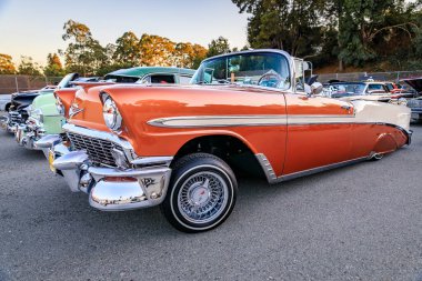 San Bruno, ABD - 7 Ekim 2022 Klasik turuncu ve beyaz 1956 Chevrolet Bel Air, krom detaylar ve kablo tekerlekleri bir araba fuarında park edilmiş.
