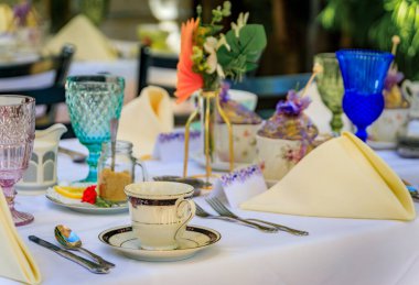 Antika çay fincanları, renkli kaprisli cam eşyalar ve San Juan Capistrano 'da bir çay partisi için katlanmış peçeteler olan açık hava restoran masası.