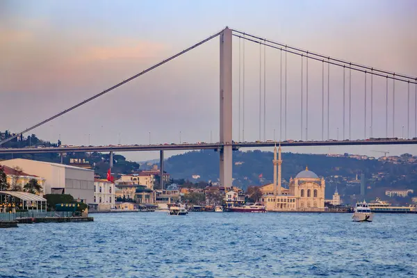 İstanbul, Türkiye 'nin alacakaranlık manzarası boğaz boyunca uzanan görkemli Boğaz Köprüsü ve rıhtım boyunca uzanan Ortakoy Camii, gün batımının altın saati