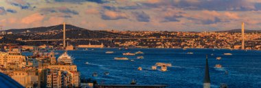 İstanbul, Türkiye 'nin ikonik şehir manzarası olan dramatik bulutlar altında altın saat günbatımında yıkanan Boğaz ve Köprü' nün panoramik manzarası