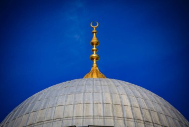 İstanbul, Türkiye 'de İslami mimarinin bir sembolü olan parlak mavi gökyüzüne karşı büyük bir cami kubbesinin tepesinde hilal ay şeklinde altın bir son