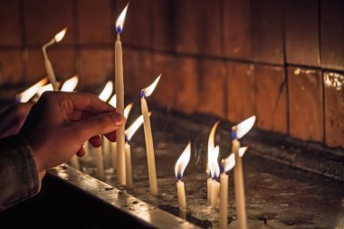 Yakın çekim bir el dikkatle titreyen bir mum yerleştirerek bir standa, diğer yanan mumlar ile çevrili loş bir ruhsal ayarda.