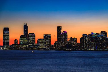 Jersey City 'nin siluetli silueti New York' tan dramatik bir günbatımı ve renkli bulutlarla New Jersey, ABD 'de Hudson Nehri üzerinde görülüyor.