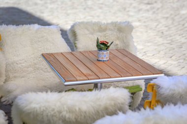 İsviçre, Zürih 'te parlak güneş ışığı altında tüylü beyaz koyun postlarıyla örtülmüş sandalyelerle çevrili Eski Şehir meydanında bir açık kafeterya masası.