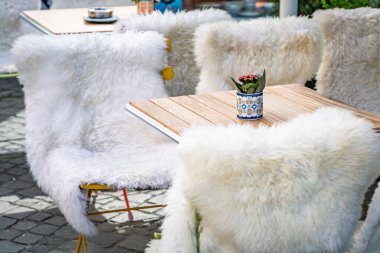 İsviçre, Zürih 'te parlak güneş ışığı altında tüylü beyaz koyun postlarıyla örtülmüş sandalyelerle çevrili Eski Şehir meydanında bir açık kafeterya masası.