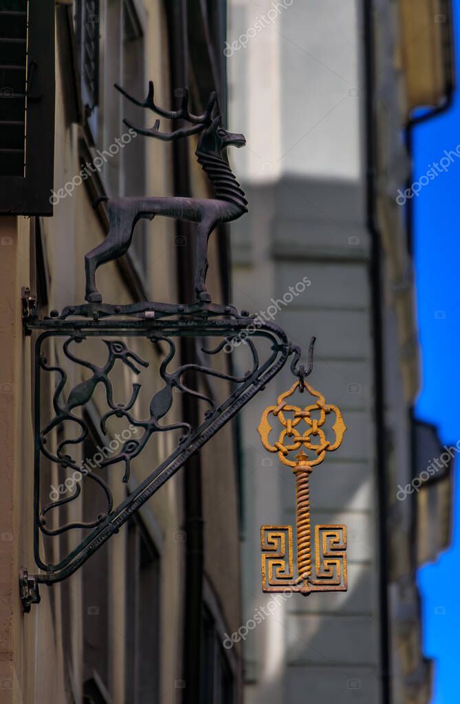 A golden ornate key hangs from an elegant wrought iron sign with a deer stag or figure in the historic Old Town or Altstadt in Zurich, Switzerland